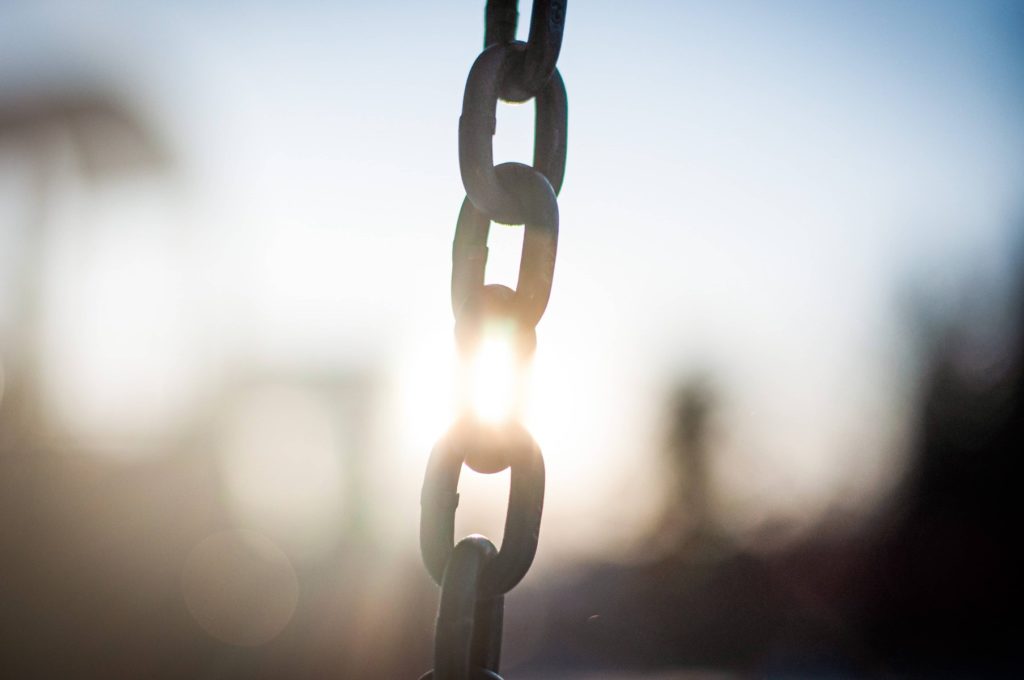 The metal links of a chain, with the sun shining behind them.