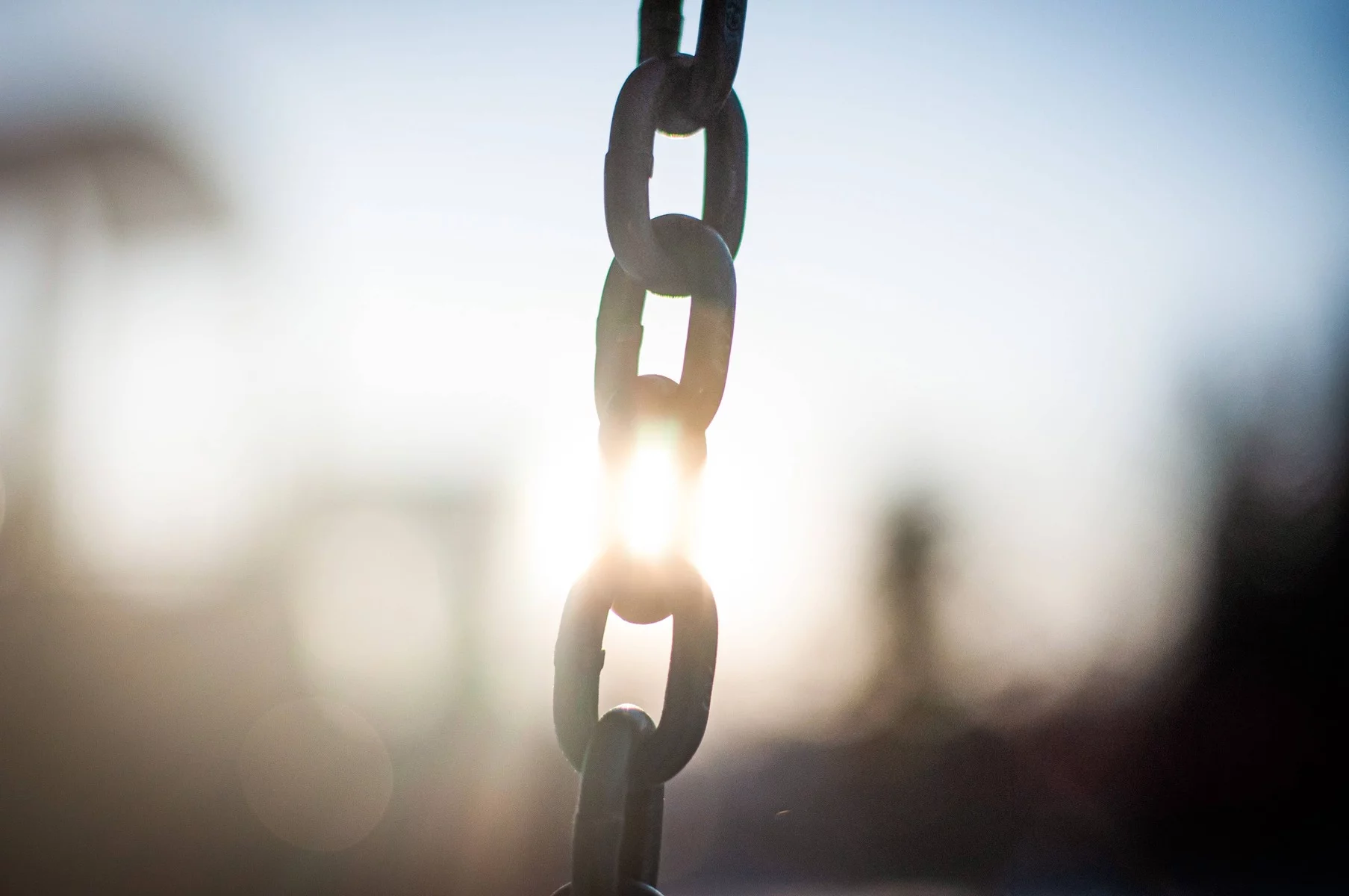 The metal links of a chain, with the sun shining behind them.
