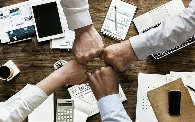 joining fists across a desk strewn with office supplies