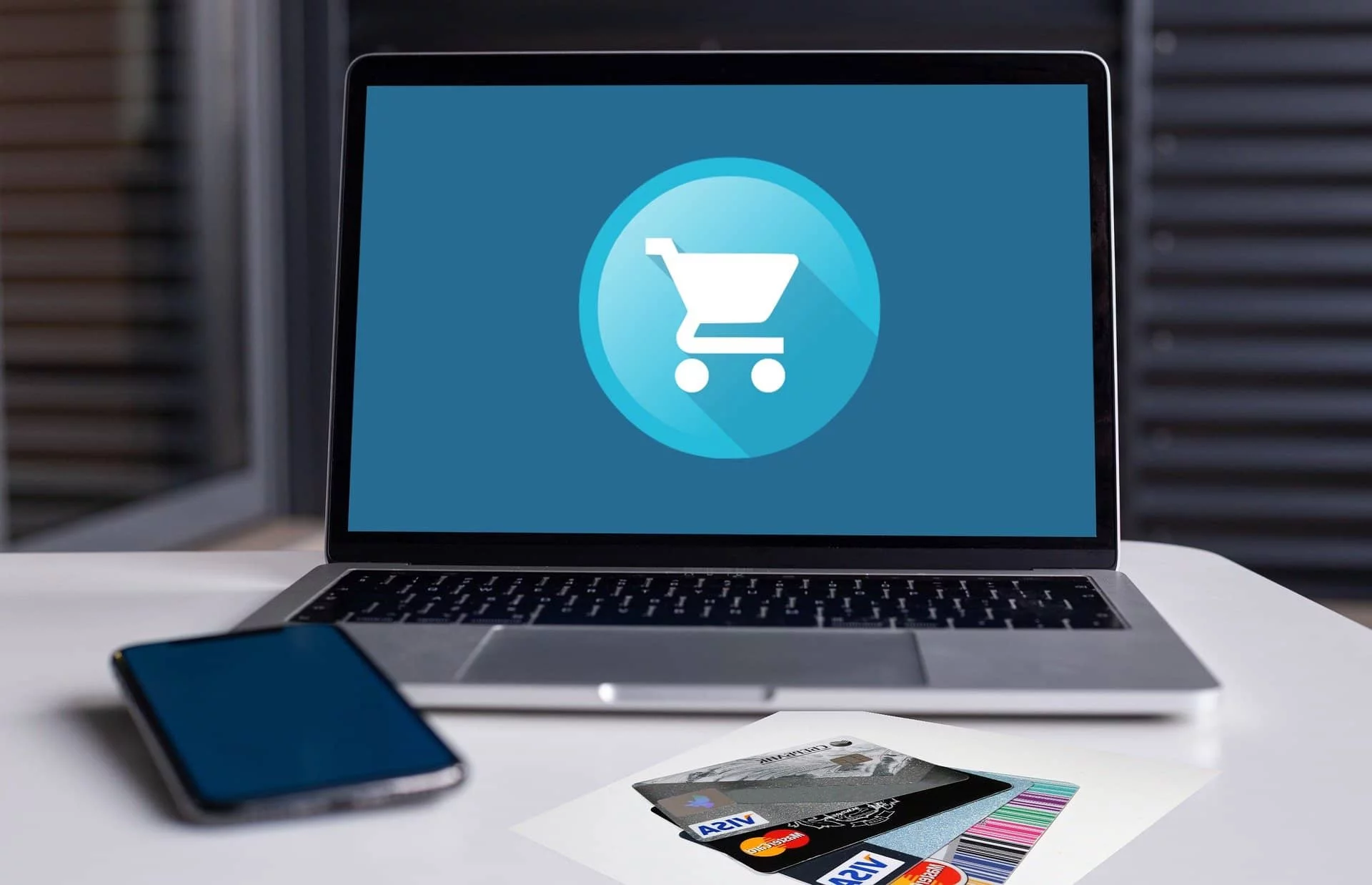 A mobile phone, a pile of credit cards, and a laptop screening showing an online shopping icon