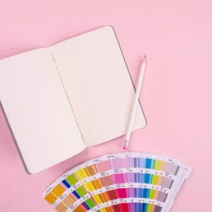 a notebook and pencil and colors on a pink background
