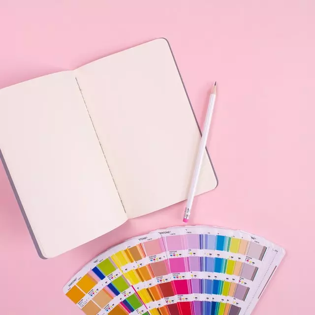 a notebook and pencil and colors on a pink background