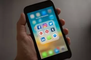 A hand holding an iPhone showing various social media platforms