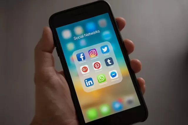 A hand holding an iPhone showing various social media platforms