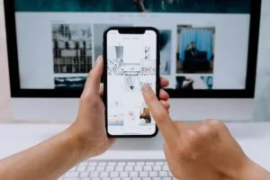a person scrolling for pictures on a phone with a computer in the background