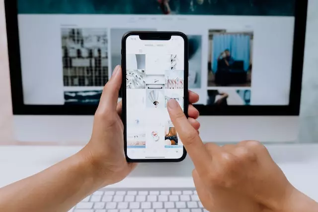 a person scrolling for pictures on a phone with a computer in the background