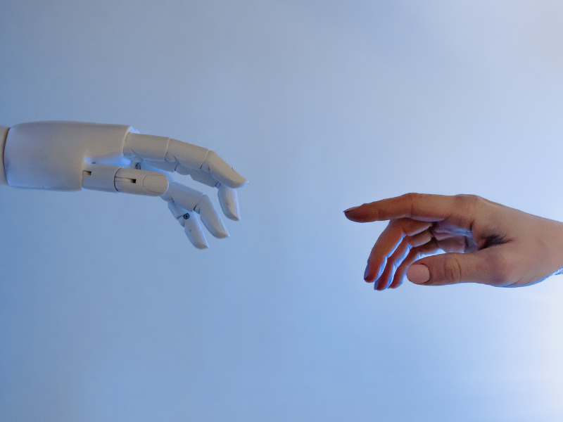 a robot hand reaching for a human hand, which is also reaching toward the robot hand